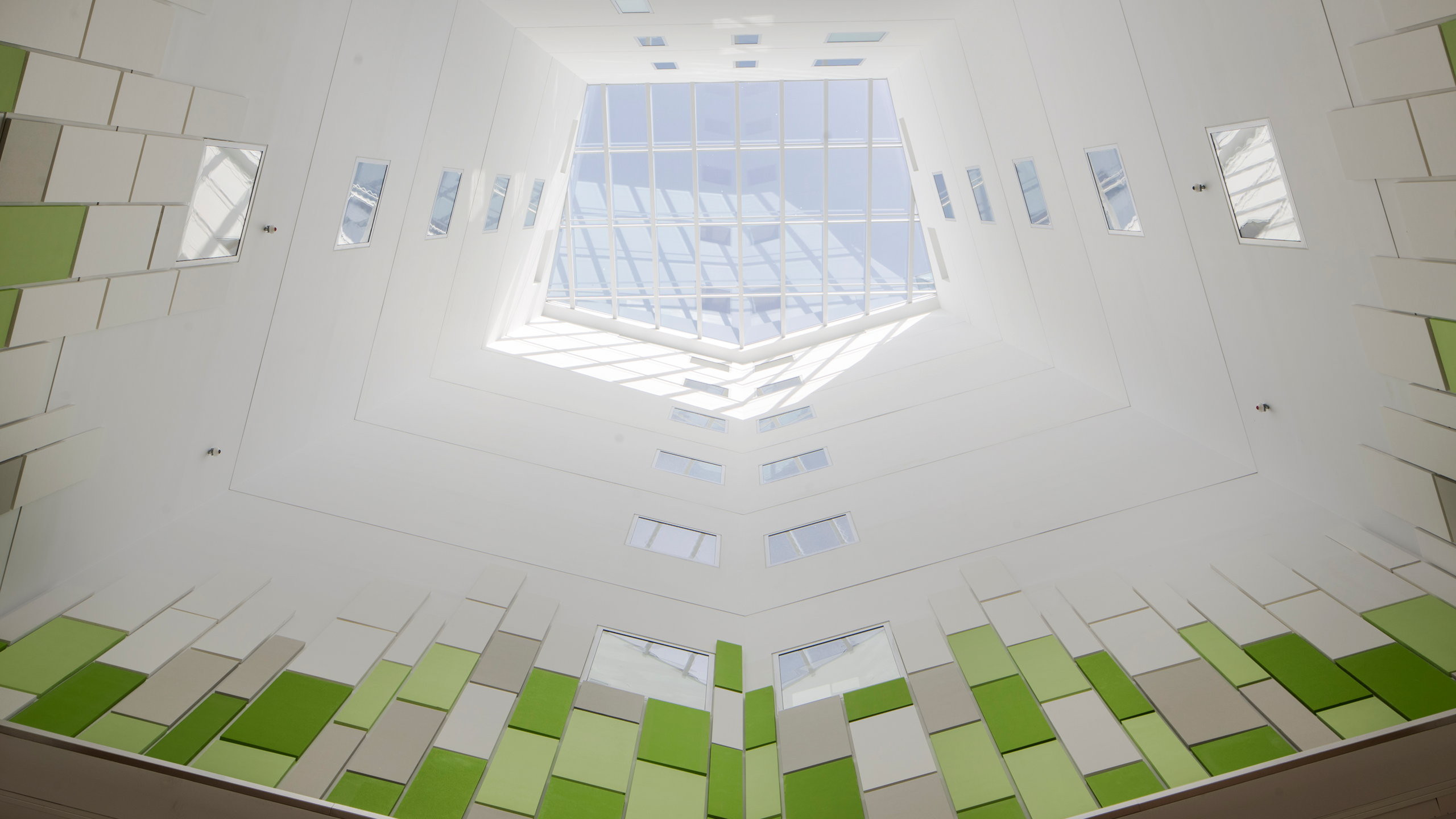 Área abierta del hospital con techo de cristal y paredes cubiertas con paneles acústicos