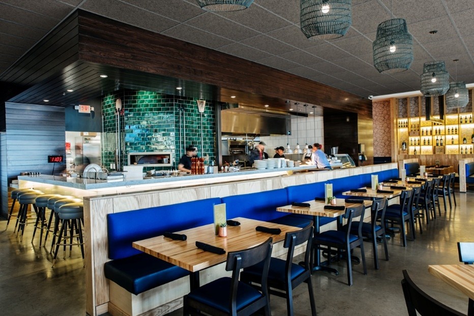Restaurant contemporain avec cuisine ouverte, murs en carrelage vert profond et banquettes bleues le long du comptoir.