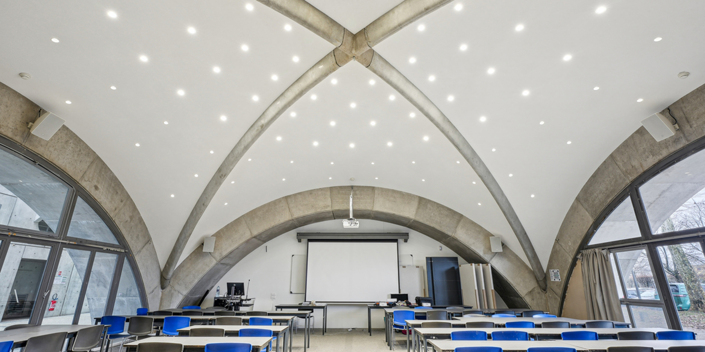 Salle moderne avec tables et chaises bleues, écran de projection et plafond voûté lumineux
