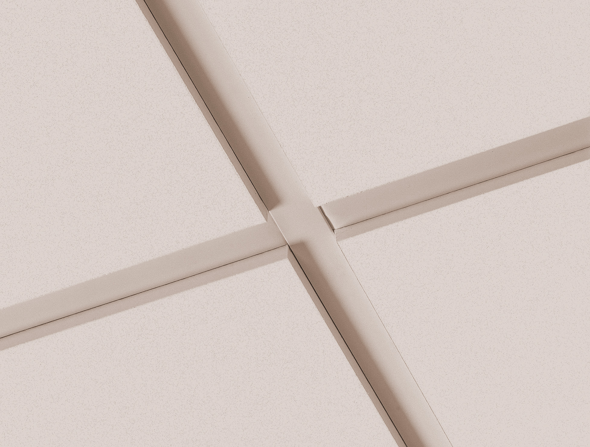 Close-up of a light pink-coloured ceiling with intersecting grid beams forming square panels. The image focuses on the intersection, highlighting clean lines and a minimalistic architectural design.
