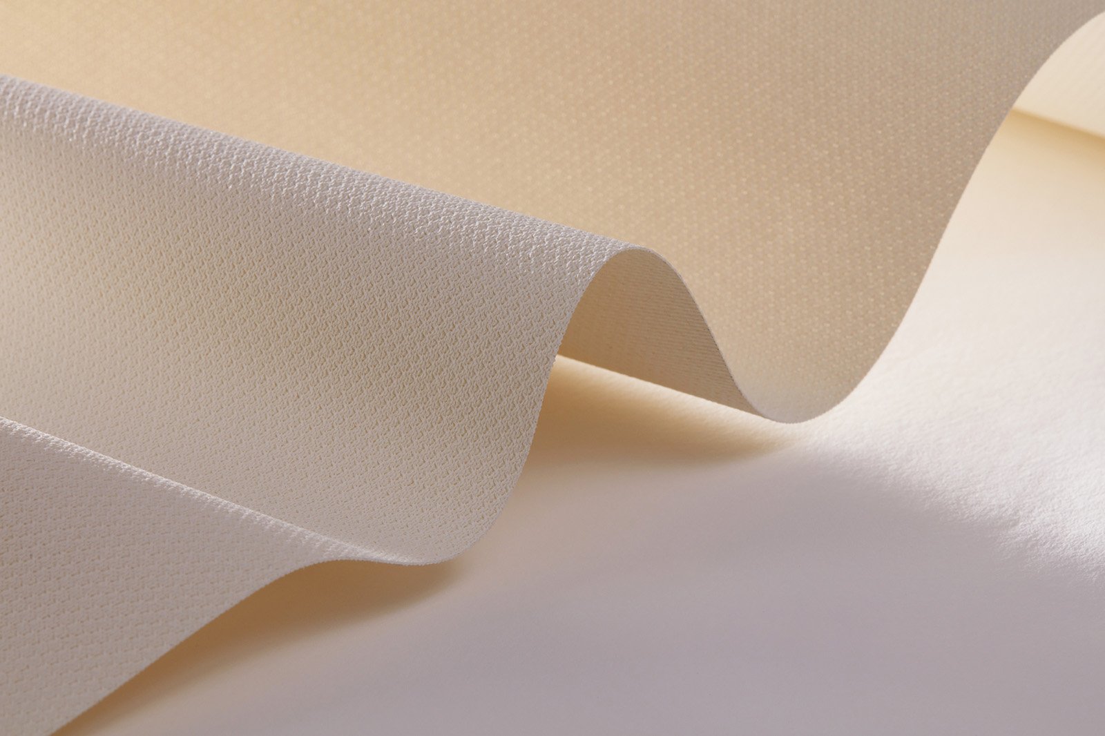 Close-up of a soft, beige fabric with a subtle wavy pattern, highlighting its texture and gentle folds. The fabric appears smooth and has a delicate sheen, catching light softly.