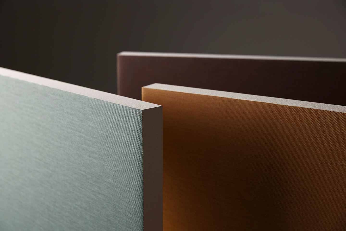Three rectangular panels in pastel green, orange-brown, and dark brown stand upright against a neutral background, showcasing different colours and textures on their surfaces.