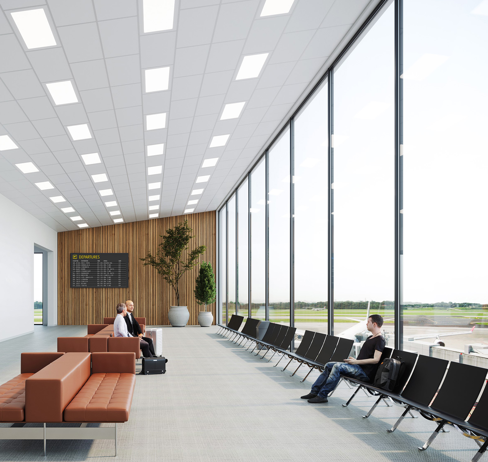 Modern airport waiting area with large floor-to-ceiling windows, brown sofas, black chairs, and a digital departures board. A man sits alone on the right whilst two people talk near luggage on the left. Aeroplanes are visible outside.