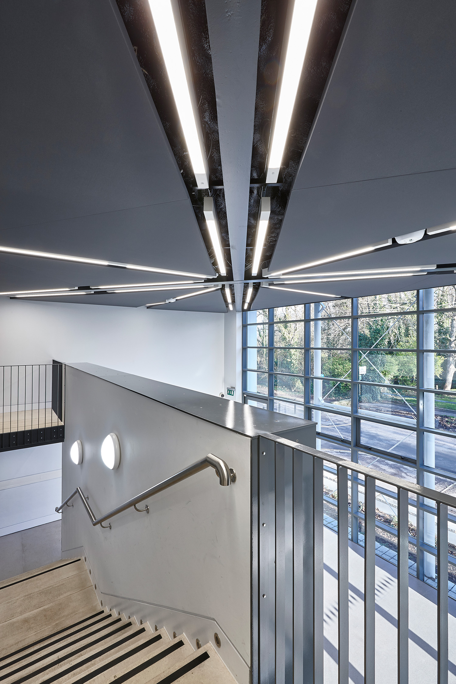 Modern, jól megvilágított belső tér, fémkorláttal és kontrasztos élekkel ellátott lépcsőházzal. A mennyezet fölött lineáris mennyezeti lámpák futnak össze. A nagy ablakokból kilátás nyílik a kinti zöldövezetre.