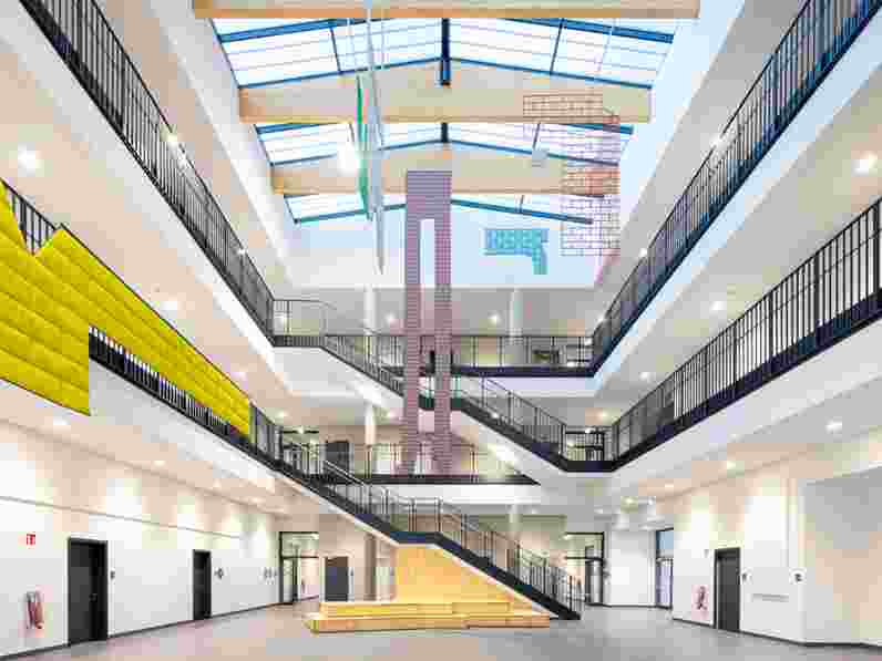 Nárazu odolný akustický strop v prostorném atriu školy s velkými barevnými dekoracemi visícími ze stropu a stěn.