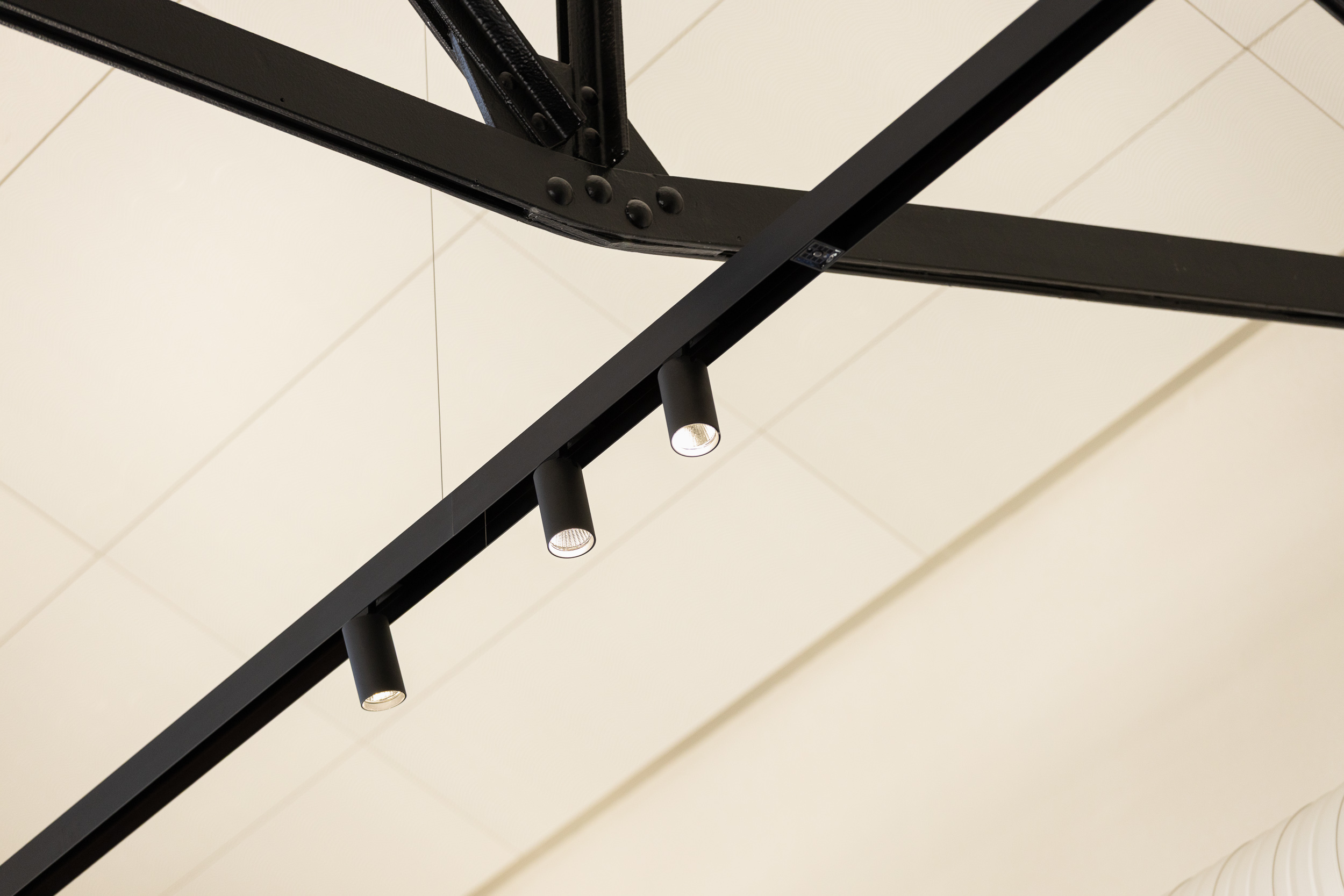 Lähikuvaa mustaan kattoristikkoon kiinnitetyistä valaisimista ja valkoisesta akustiikkakatosta