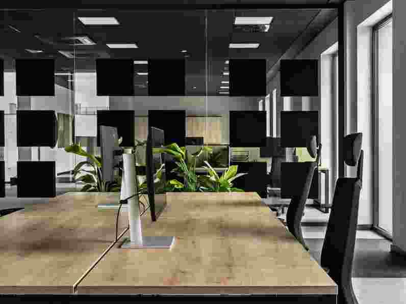 Black, suspended acoustic ceiling in open-plan office with glass wall dividers with black details and a close-up of a work station with wooden desks.