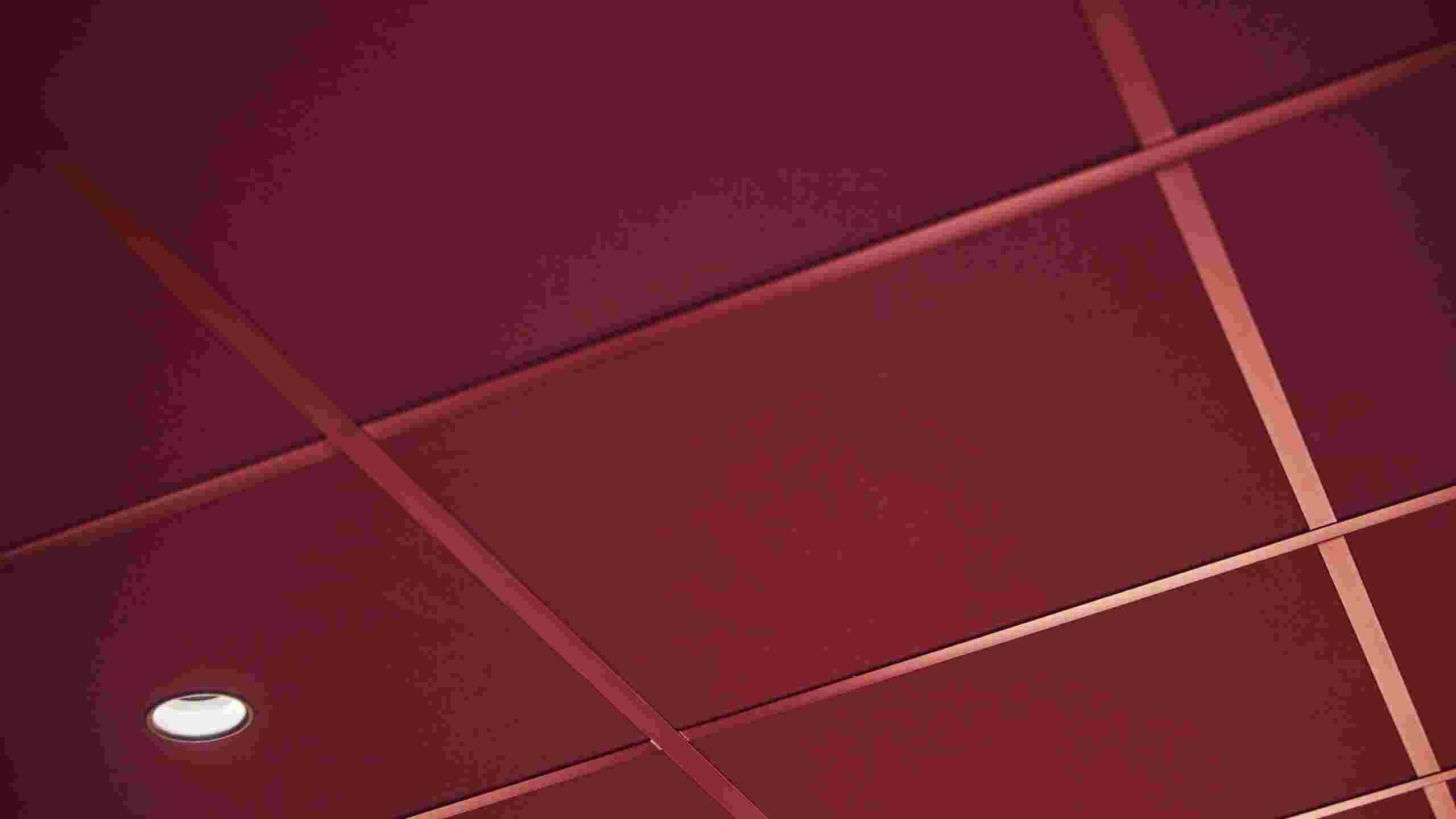 Close-up of dark red suspended acoustic ceiling with matching grids