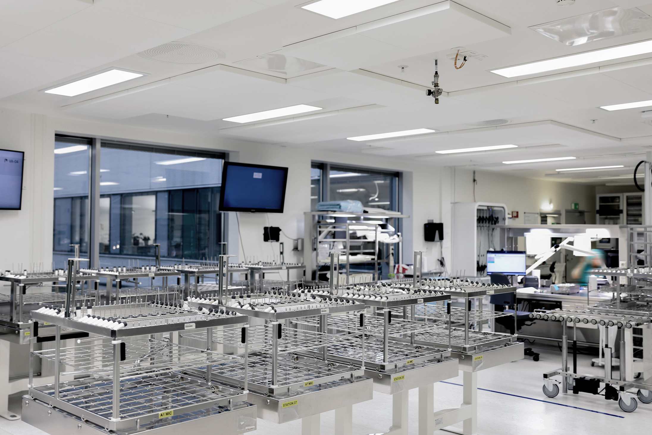 A modern, clean laboratory with empty stainless steel racks, large windows, computer monitors, and various equipment. The space appears organised and brightly lit, suggesting a sterile work environment.