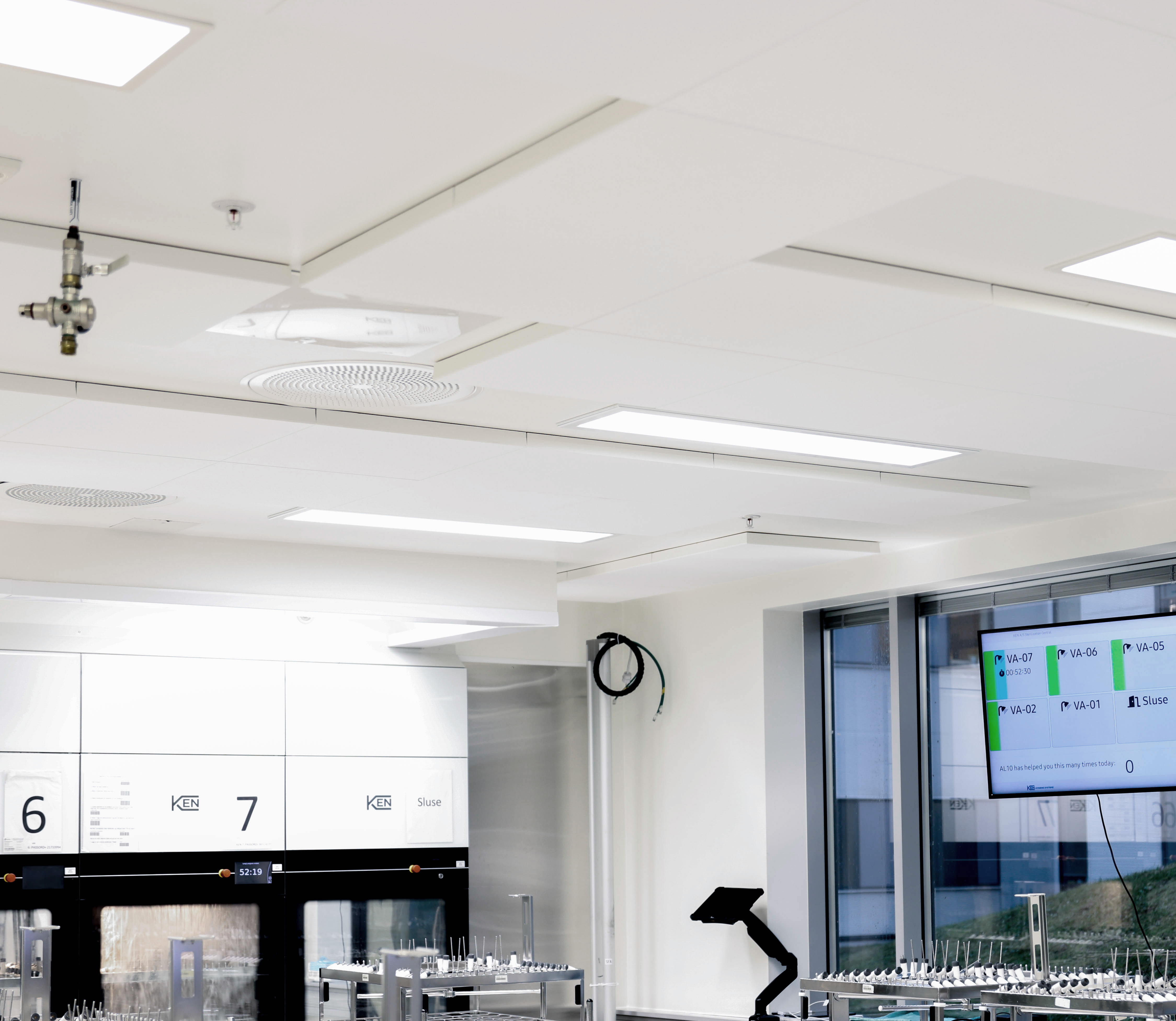 A modern, sterile laboratory with bright overhead lighting, white walls, digital displays, and stainless steel equipment. The room appears organised with clean workstations and large windows.