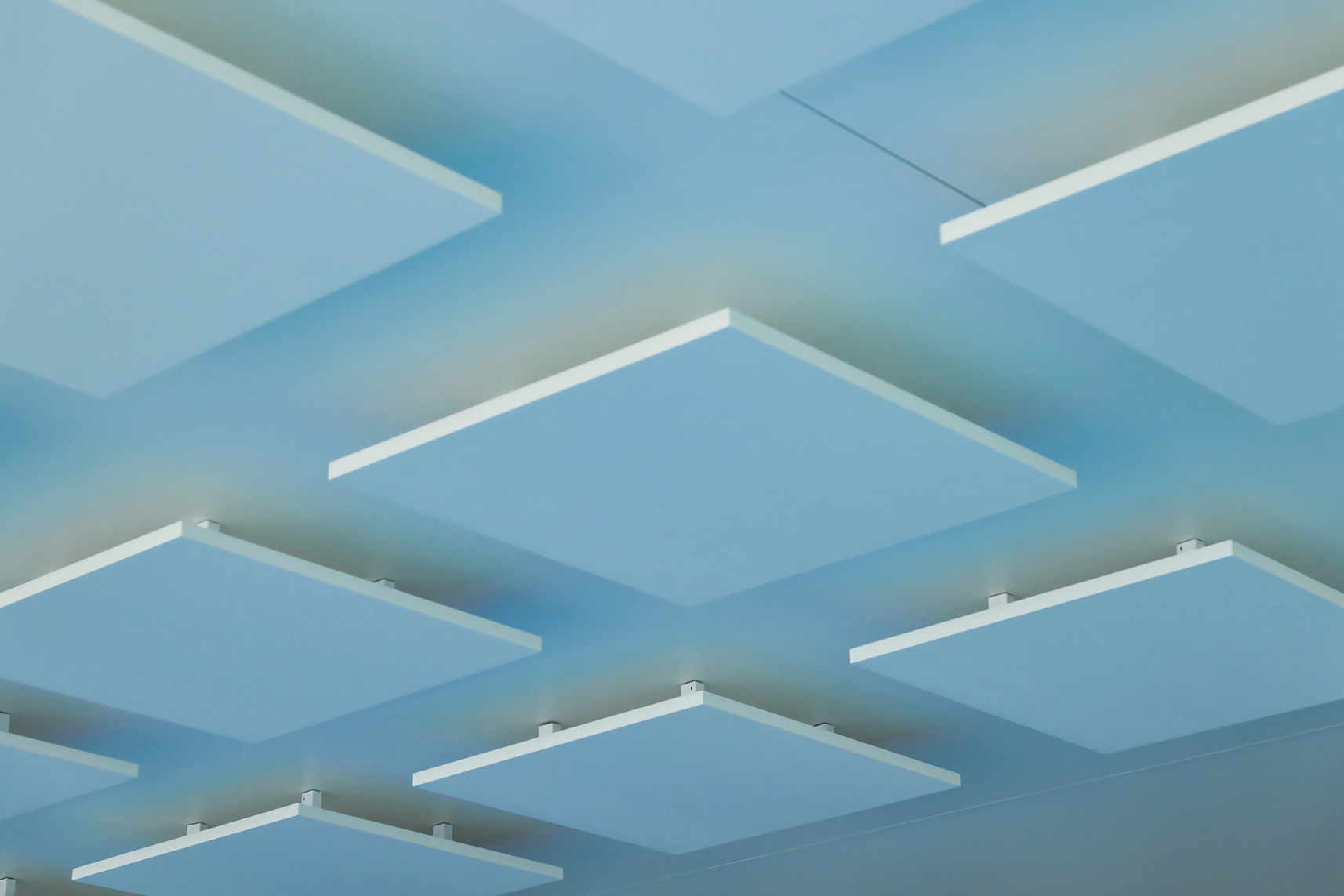 Blue ceiling with evenly spaced, rectangular white acoustic panels arranged in a grid pattern, creating a modern and geometric appearance.
