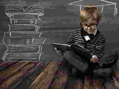 Boy with glasses reading a book in front of a blackboard