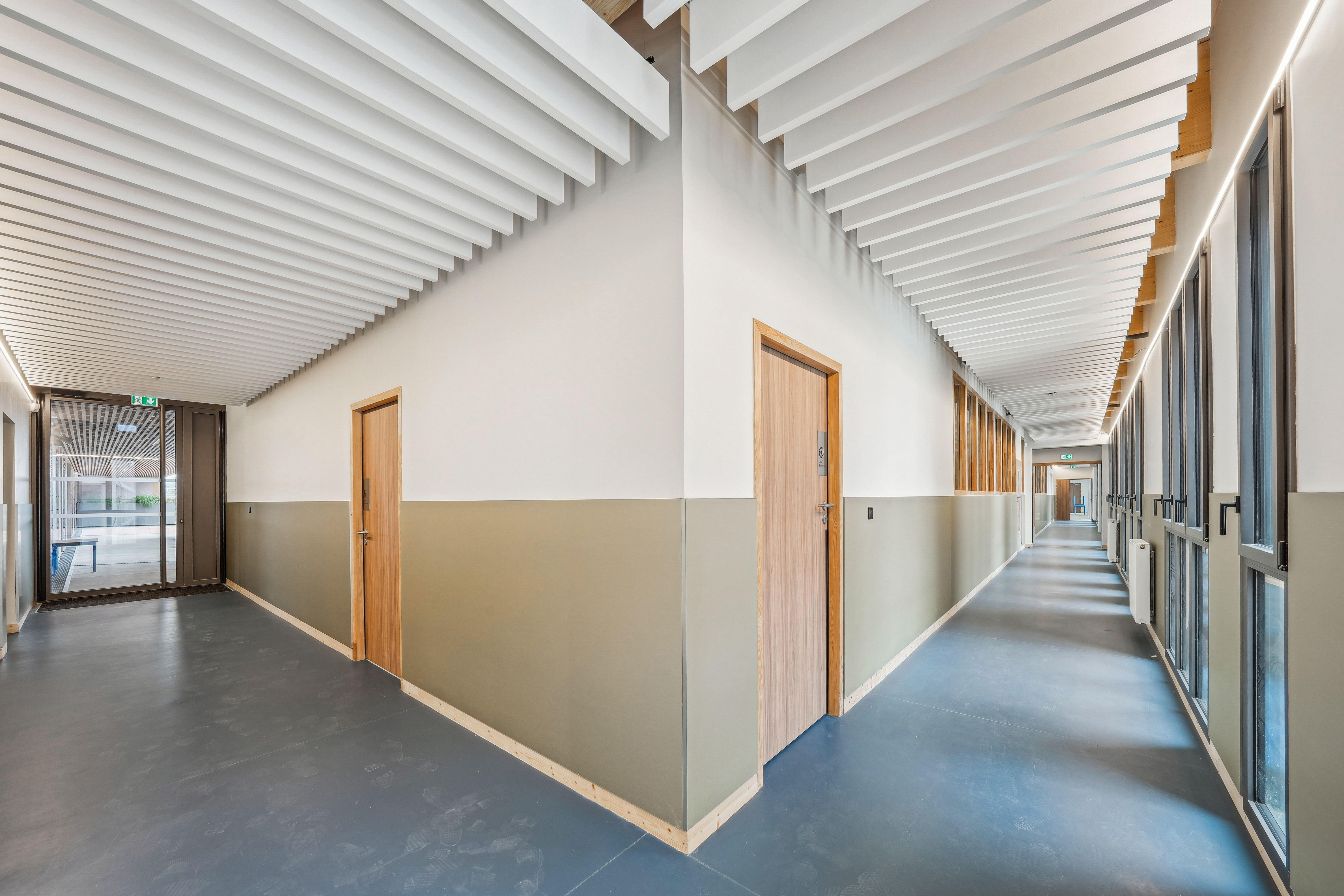 Photo prise dans l'angle d'un couloir de l'école avec des baffles acoustiques blanches au plafond