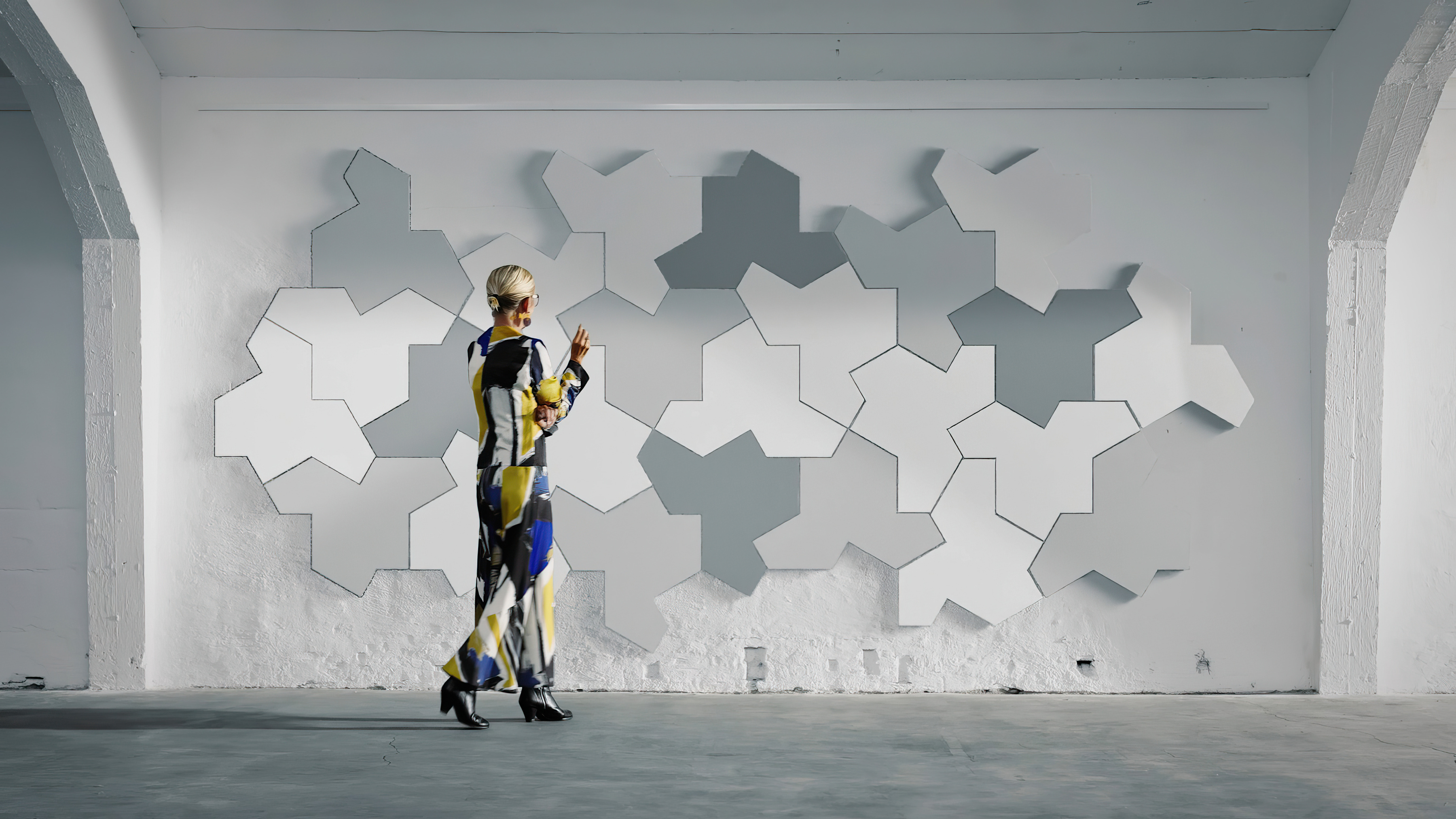 Woman in colourful dress standing in front of a concrete wall covered with white and grey acoustic wall panels in jigsaw pattern