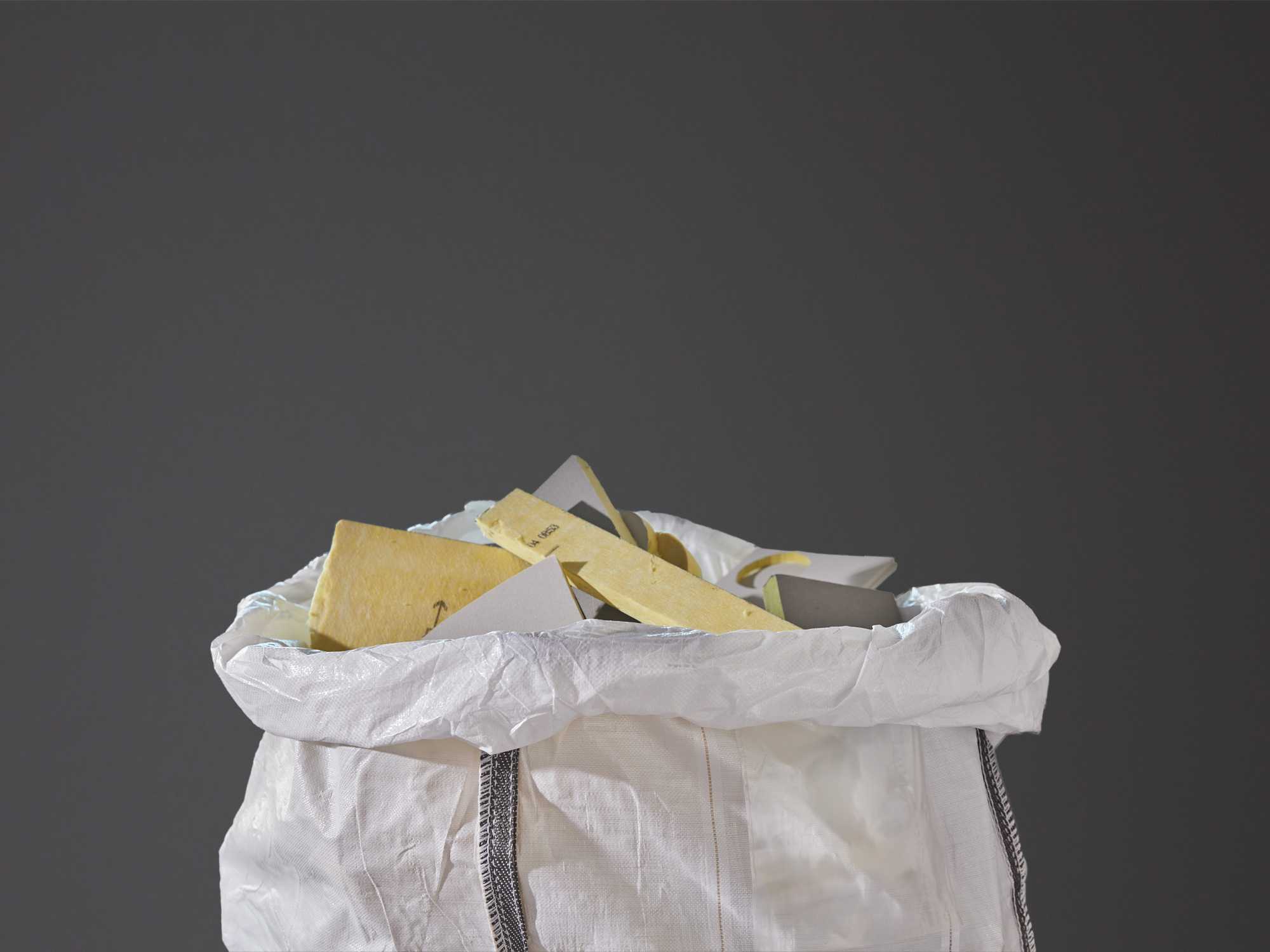 Close-up of a white plastic bag filled with used acoustic glasswool panels