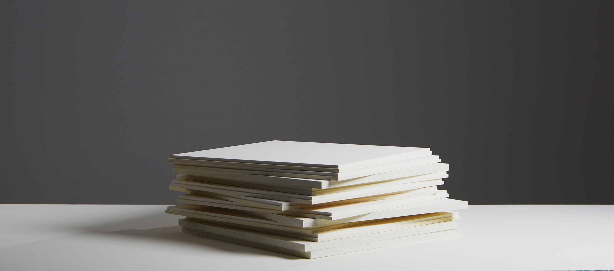 A pile of white acoustic panels lying on a white surface and a dark grey background